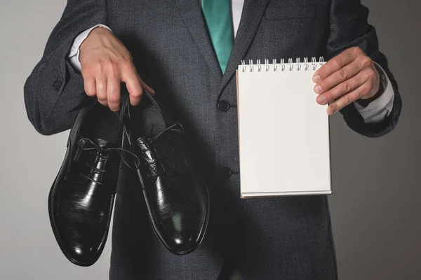Shoe care tips mock up. Business man holding in hands a new pair of black shoes and a blank page notepad with a copy space.