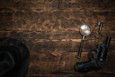 Dedektif ya da casus ajan, ahşap masa, arka planda fotokopi alanı var. Tabanca, siyah deri şapka, büyüteç ve çalışma masasında paslı bir anahtar..