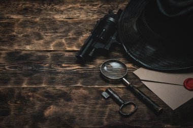 Çok gizli bir zarf, tabanca, deri şapka, anahtar ve büyüteç..