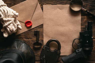 Çok gizli bilgi modeli, deri şapka, silah, büyüteç ve halat gizli servis ajanının ahşap masasında düz bir zeminde yatıyordu..