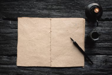 Boş bir sayfa kitabı, bir kopya alanı ve siyah ahşap bir masa üzerinde bir tüy kalem arka planda yatıyordu..