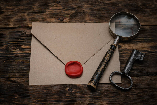 Old envelope with a sealing wax stamp, rusty key and a magnifying glass on a brown wooden table background with a copy space.