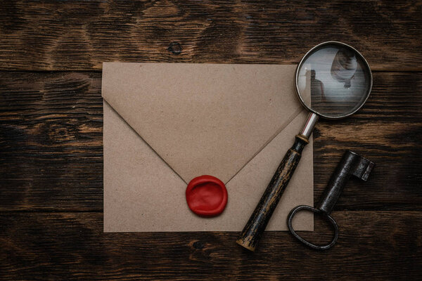 Old envelope with a sealing wax stamp, rusty key and a magnifying glass on a brown wooden table background with a copy space.