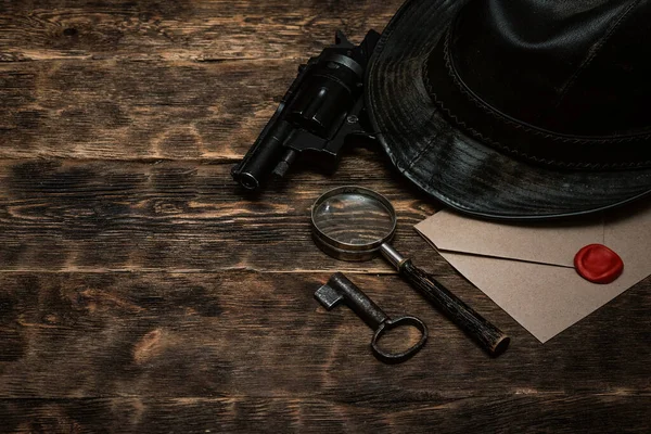 Top secret envelope, gun, leather hat, key and magnifying glass on a wooden table of detective agent table background.