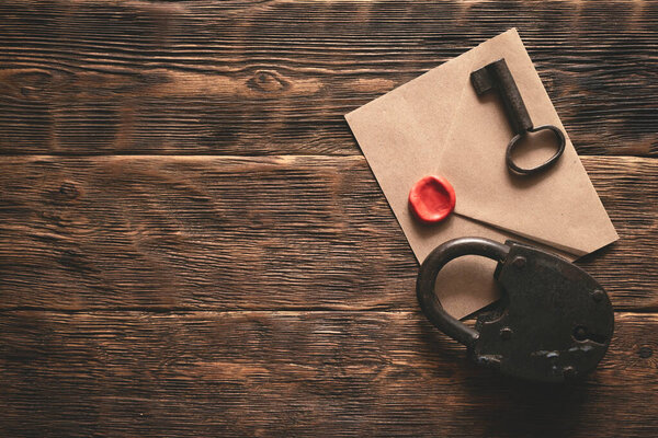 Top secret documents in envelope, rusty padlock and a key on a wooden table flat lay background. Confidential information concept.