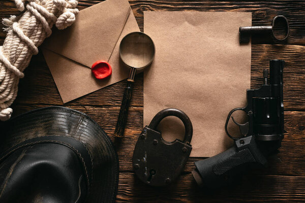 Top secret information mockup, leather hat, weapon, magnifying glass and rope on a wooden table of secret service agent flat lay background.