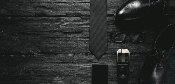 Бизнес-квартира лежала на заднем плане с копировальным пространством. Мужская обувь, ремень, мобильный телефон, очки и галстук на черном деревянном полу
.