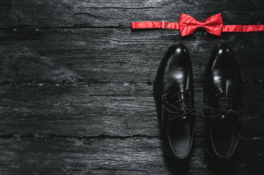 Erkek ayakkabıları ve kırmızı fiyonk siyah ahşap bir zeminde. Kopya alanı olan düz iş arkaplanı.