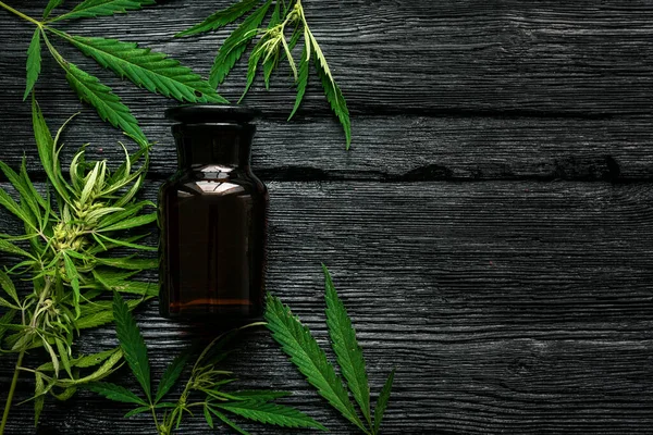 Cannabis cbd oil in bottle and green leaves on a black wooden table flat lay background.