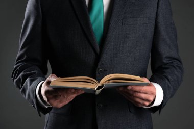 İşadamı elinde gri bir arka plan üzerine bir kitap okuyor. İş eğitimi. Hesap Defteri.