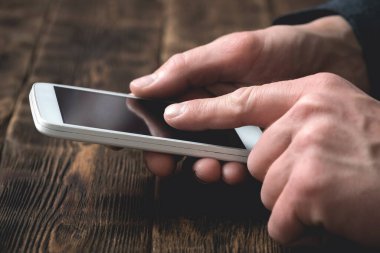 Boş ekranlı cep telefonu iş adamının elinde eski bir ofis masasının arkasında. Bizimle irtibata geç..