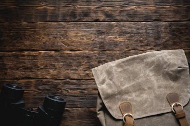Seyahat ya da macera düz arka plan fotokopi alanı ile yatıyordu. Kahverengi ahşap bir masada bir sırt çantası ve bir dürbün..
