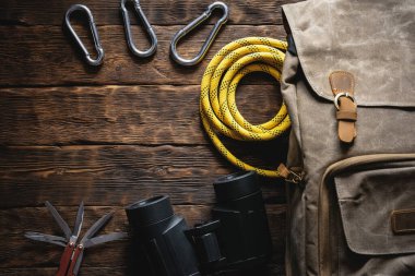 Seyahat ya da macera düz arka plan fotokopi alanı ile yatıyordu. Sırt çantası, çoklu alet bıçağı, ip, karabina ve kahverengi ahşap bir masada dürbün..