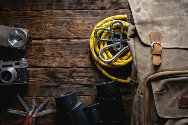 Seyahat ya da macera düz arka plan fotokopi alanı ile yatıyordu. Sırt çantası, fotoğraf makinesi, el feneri, çoklu alet bıçağı, ip, karabina ve kahverengi ahşap bir masada dürbün..