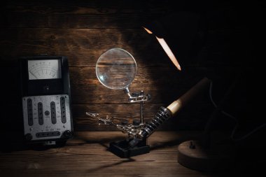 Retro analog voltmetre ve lamba ışığında lehim demiri kahverengi ahşap masa arkasında. Elektrik işleri soyut arkaplan. 