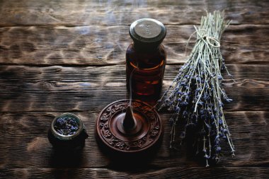 Ahşap masa arkasında kurutulmuş lavanta çiçeği dalları ve lavanta yağı şişeleri. Bitkisel ilaç ya da aromaterapi konsepti.