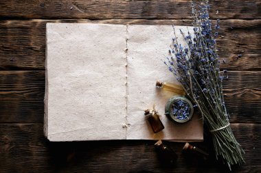 Kurutulmuş lavanta çiçeği dalları, lavanta yağı şişeleri ve boş aromaterapi tarifi kitabı fotokopi alanı olan ahşap bir masa arkaplanı üzerine yazılmış. Bitkisel tıp konsepti.