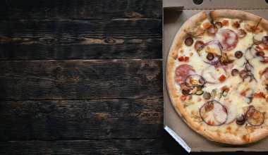 Kahverengi ahşap bir masa zemininde, karton bir kutuda peynirli ve sosisli taze pizza..