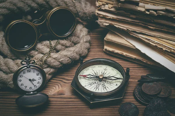 Seyahat ya da macera geçmişi. Macera masası. Dürbünler, eski kitaplar, demirleme halatı, pusula, antik paralar ve masanın üzerinde bir cep saati..