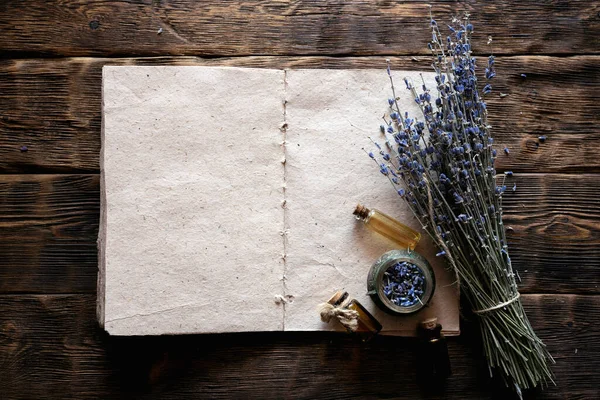 Dried lavender flower branches, lavender essential oil bottles and a blank aromatherapy recipe book mock up on a wooden table background with copy space. Herbal medicine concept.