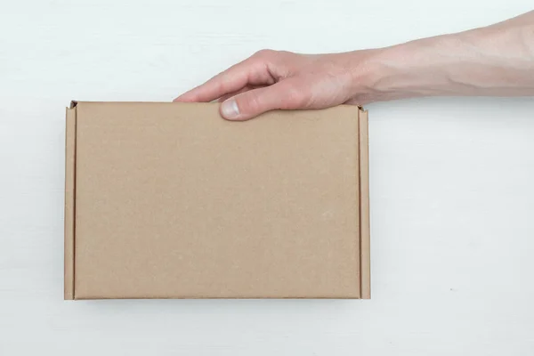 白い木製のテーブルの背景に配達人の手に小包段ボール箱 配送サービスのコンセプト — ストック写真
