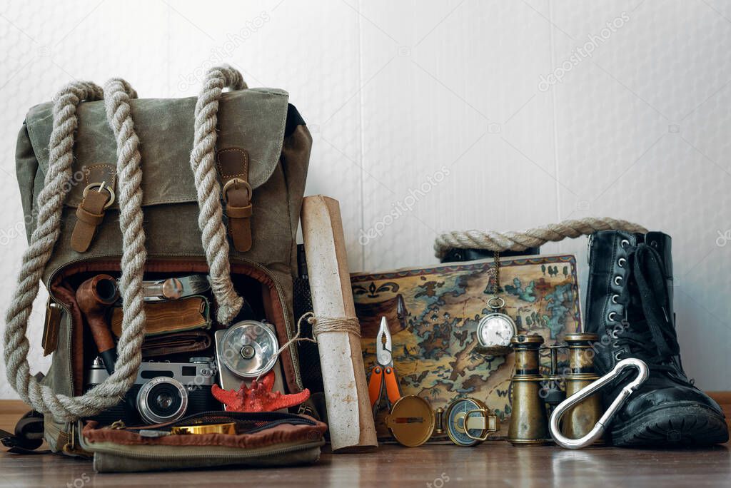 Travel or adventure background. Treasure map, backpack, boot, binoculars, compass, pocket watch, rope and photo camera on a floor on a white wall background .