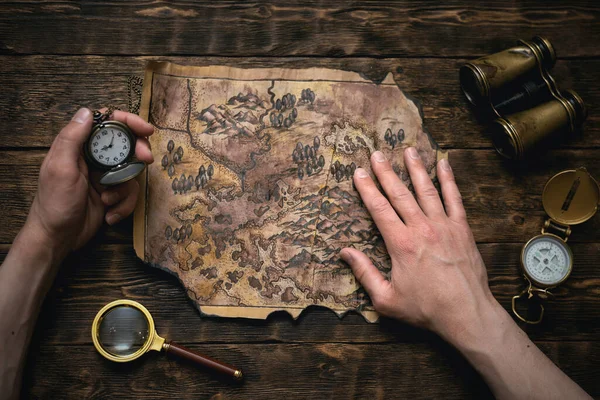 Old map in man adventurer hands on a brown table background. Treasure hunt concept.