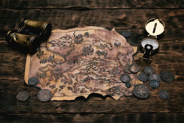 Old map, compass and binoculars on a adventurer table background. Treasure hunt concept.