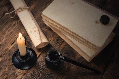 Kitap, tükenmez kalemli mürekkep hokkası ve yazar tahtası arka planında eski bir parşömen belgesi.