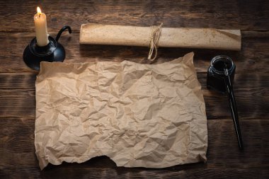Fotokopi alanı olan boş kağıt parşömen, kalem ve yanan mum ahşap masa arkasında. Hazine haritası modeli.