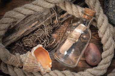 İçinde korsan hazine haritası olan bir şişe, kahverengi ahşap masa zemininde demirleme yerleri ve deniz kabukları..