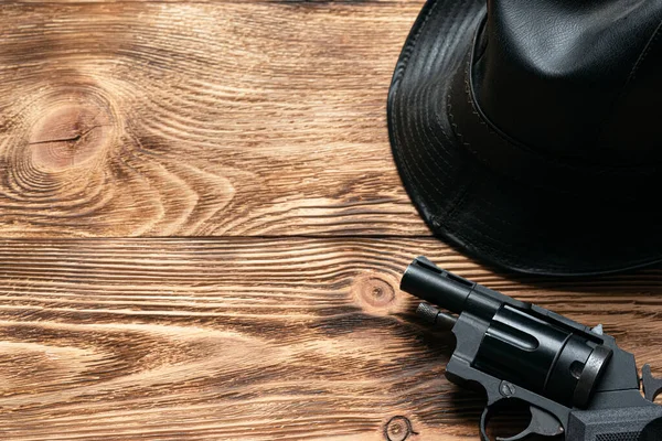 Gun and leather black hat on detective agent wooden tabe background with copy space.