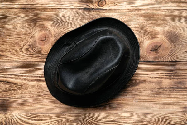 Black leather hat on a brown wooden table flat lay background.