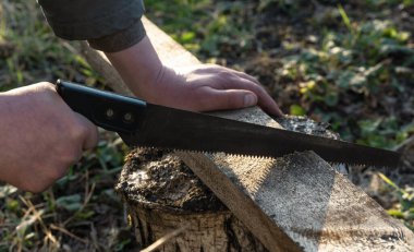 Adam arka bahçede el testeresiyle çalışıyor..