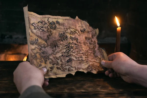Adventurer man is holding in hands a treasure map over a burning fire background. Treasure hunt concept.