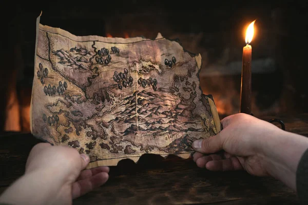 Adventurer man is holding in hands a treasure map over a burning fire background. Treasure hunt concept.