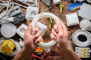 Elektrikçi ahşap tezgahta çeşitli elektrikli ekipman arka planında bir kablo tutuyor..
