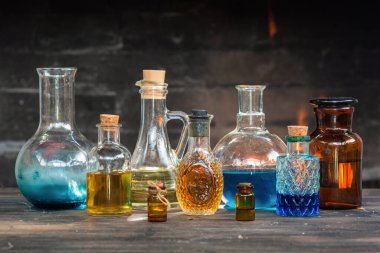 Renkli sihirli iksir şişeleri ahşap masada şömine arkasında yanan ateşin üzerinde. Cadı doktor masası..