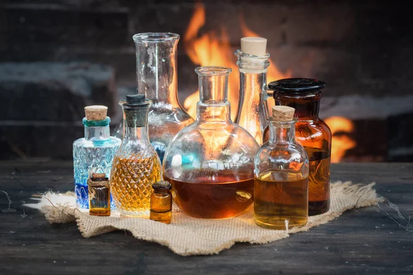 Colorful magic potion bottles on wooden table on burning fire in fireplace background. Witch doctor table.