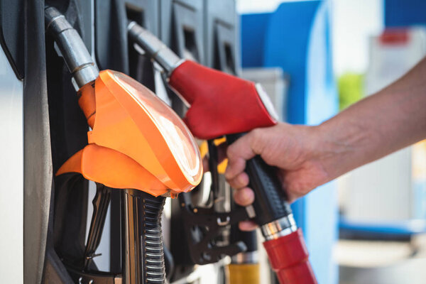 Man is holding a fuel nozzle close up on the gas station.
