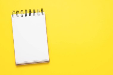 Sarı düz arkaplandaki boş not defteri sayfası kopya alanı ile yatıyordu.