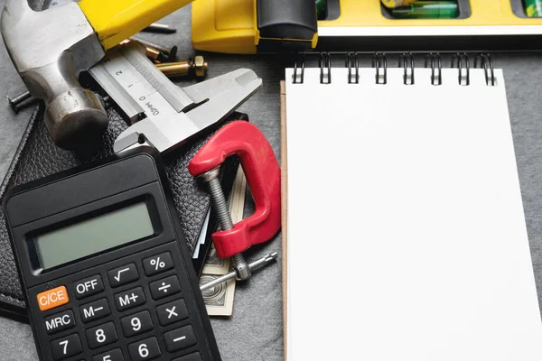 Construction cost or repair calculation mockup. Blank page notepad and work tools on the workbench.