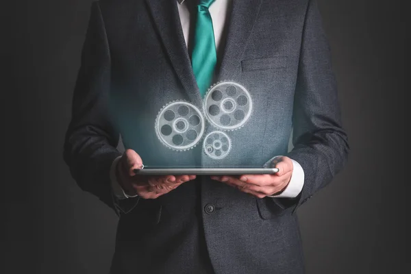 Businessman with digital tablet in hands with gear wheels projection above.