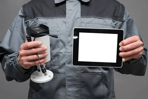 CCTV installation worker with a security camera and blank screen digital tablet close up.