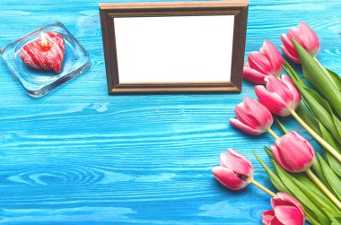 Lale çiçekleri ve sevilen bir fotokopi alanının boş fotoğraf çerçevesi ve mavi ahşap masa zemininde yanan mum. Kadın günü konsepti. Anneler Günü geçmişi. Sevgililer Günü tebrik kartı maketi. Üst görünüm.