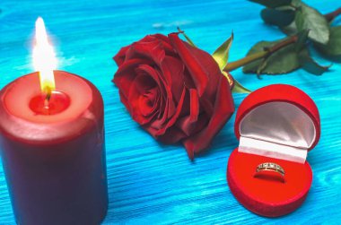 Wedding ring in a gift present box red rose flower and burning candle on wooden table background. Marriage offer romantic background. The proposal concept. clipart