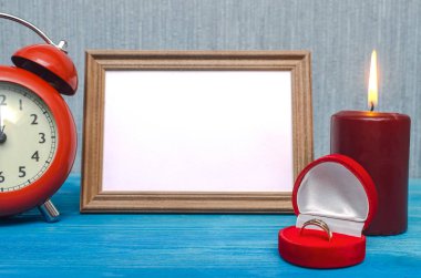 Wedding ring in a gift present box and empty photo frame of a loved one copy space and red alarm clock on wooden table background. Marriage offer template. The proposal concept. clipart
