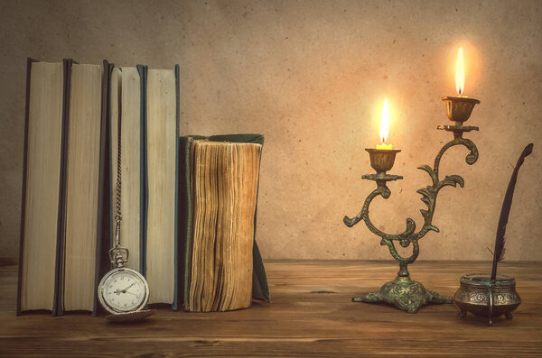 Old book and feather pen with inkpot and rusty key on retro wooden table background in the light of burning candle. Education. Back to school. Memoirs. Writer table concept. Vintage background.