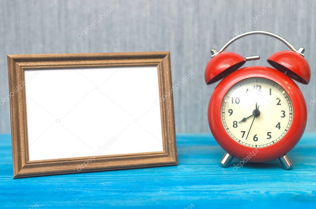 Retro red alarm clock and photo frame with copy space on wooden table surface background. Nostalgia. Awakening time. Eight hours. In expectation of something concept.
