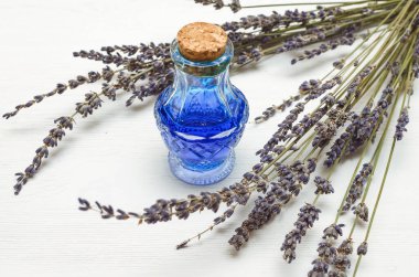 Kuru lavanta dalları ve beyaz ahşap arka planda mavi tıbbi tentürle dolu bir şişe. Bitkisel tıp konsepti. Alternatif tıp.